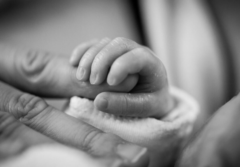 black and white image showing a baby's hand curled around an adult sized finger